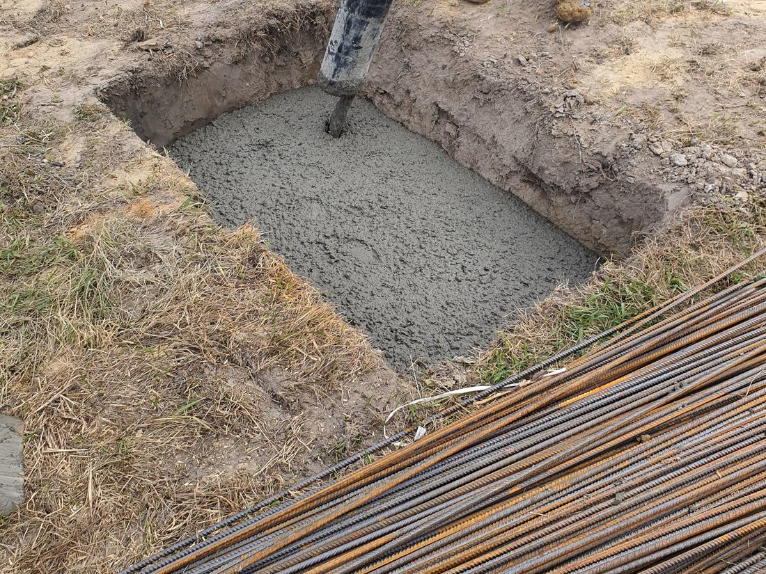 A foundation filled with fresh concrete, with reinforcing bars on the ground beside it